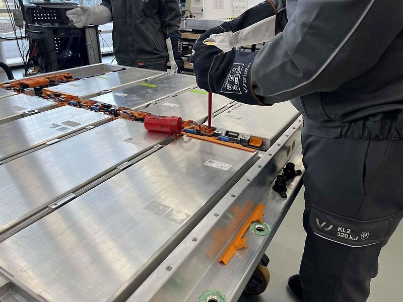 Vyjmutá baterie z vozu, ležící na hydraulickém stole a propojená s vozem prodlužovacími kabely
