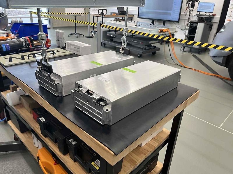 Vyjmutá baterie z vozu, ležící na hydraulickém stole a propojená s vozem prodlužovacími kabely