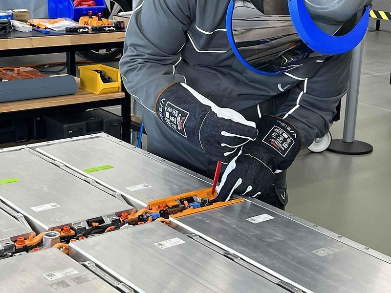 Vyjmutá baterie z vozu, ležící na hydraulickém stole a propojená s vozem prodlužovacími kabely