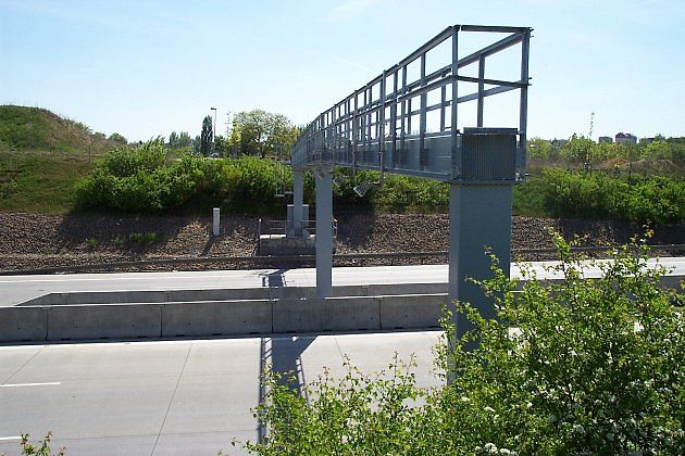 Moderní sledovací systémy bývají nenápadně umístěné na mýtných branách nebo konstrukcích nad silnicí. Z vyvýšeného místa vidí přes čelní sklo přímo do kabiny vozidla., zdroj: Aktron/Wikimedia CC BY 3.0