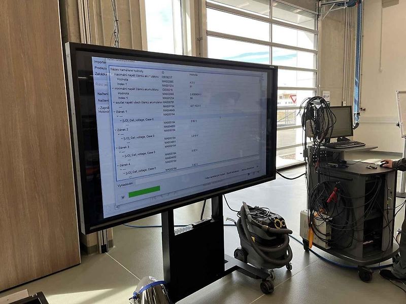 Vyjmutá baterie z vozu, ležící na hydraulickém stole a propojená s vozem prodlužovacími kabely