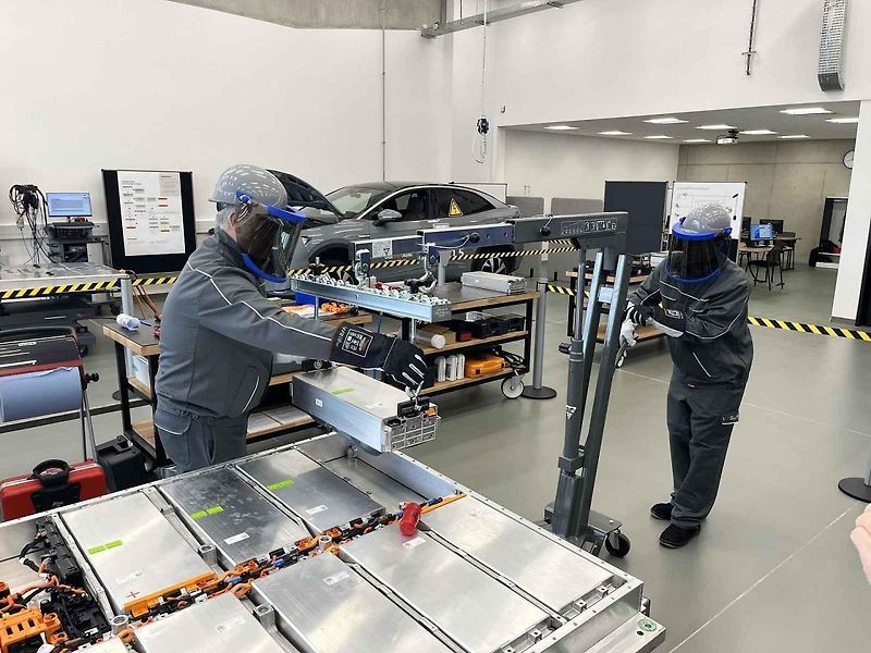Vyjmutá baterie z vozu, ležící na hydraulickém stole a propojená s vozem prodlužovacími kabely