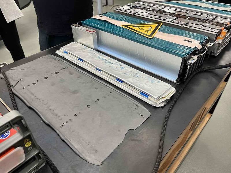 Vyjmutá baterie z vozu, ležící na hydraulickém stole a propojená s vozem prodlužovacími kabely