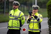 Policista v uniformě obsluhuje ruční laserový měřič rychlosti, jehož signál se zakázané aktivní antilasery snaží neúspěšně rušit.