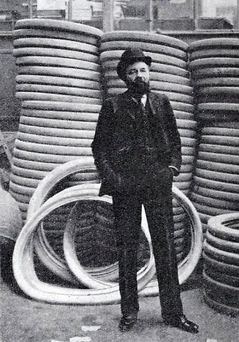 André Michelin před výrobky své firmy, automobilovými pneumatikami, v roce 1904., zdroj: Wikimedia Commons, La Vie au Grand Air, volné dílo