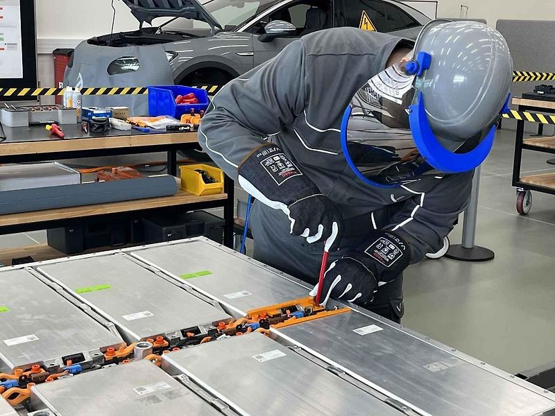 Vyjmutá baterie z vozu, ležící na hydraulickém stole a propojená s vozem prodlužovacími kabely