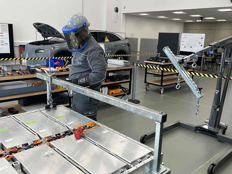 Vyjmutá baterie z vozu, ležící na hydraulickém stole a propojená s vozem prodlužovacími kabely