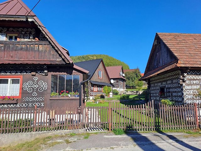 Pohled do jedné z uliček památkové rezervace lidové architektury s malovanými dřevěnicemi a hřebenem Strážovských vrchů v pozadí.  Foto:  Se svolením Petra Kučery